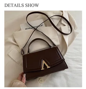 Détail du sac à main en cuir marron foncé avec boucle métallique en V doré et rabat