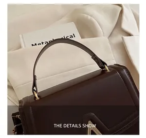 Détail d'un sac à main carré marron foncé avec ferrures dorées et texture lisse