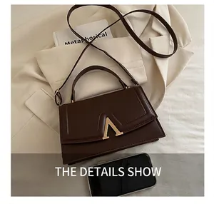 Détail du sac à main marron avec boucle dorée en V sur une veste beige chic