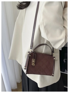 Detail of dark brown quilted leather bag with turn-lock clasp on a beige blazer background