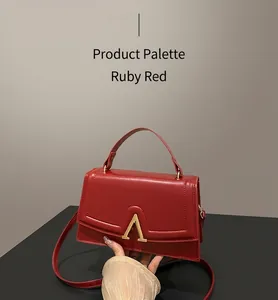 Détail du sac à main rouge en cuir avec fermoir doré en V sur une table en bois