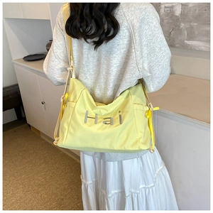 Detail view of the yellow canvas tote bag showing the 'Hai' embroidery on a person's back