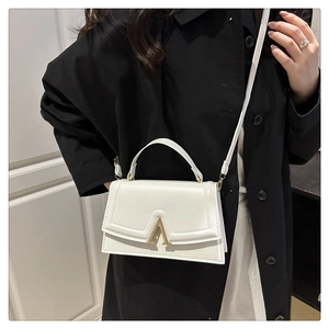 Close-up of cream square crossbody bag featuring a golden A-shaped metal clasp and flap