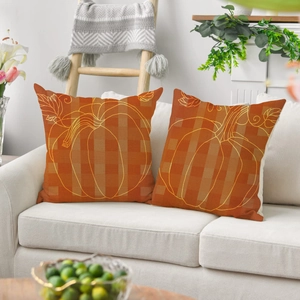 Detail of two orange linen pillow covers with golden pumpkin outlines on a sofa