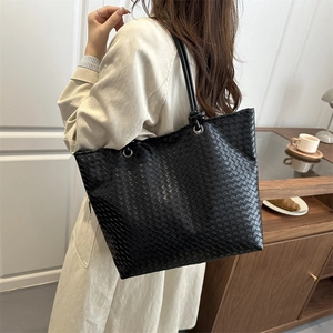 Large black woven leather tote bag for women with minimalist shoulder straps on a model