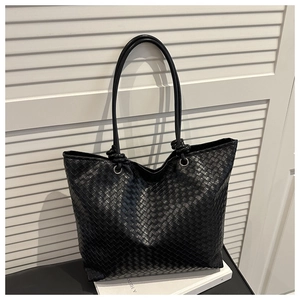 Close-up of the black woven tote bag showing intricate cross-weave texture and metal rings