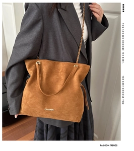 Detailed close-up of brown suede tote bag featuring gold chain strap and metal logo