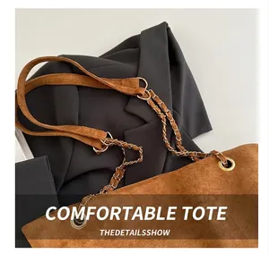 Detail of brown suede shoulder bag with metal chain strap on a black blazer