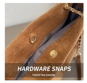 Close-up of golden magnetic buckle on brown suede bag with premium metal chain details