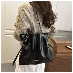 Detail of black pleated bucket bag with gold chain strap and FASHION metal logo