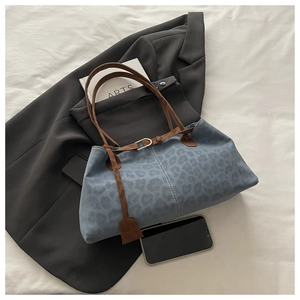 Flat lay of large blue leopard print tote bag with brown straps on a grey blazer