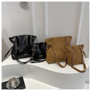Detail of black faux leather and brown suede tote bags with chain straps on white stairs
