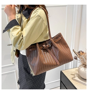 Detail of a large brown woven tote bag featuring a leather strap and buckle on a model