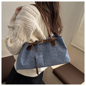 Detail of blue leopard print tote bag featuring brown leather straps and gold buckle