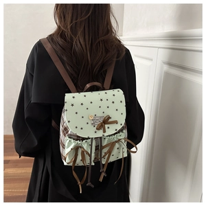 Detail showing checkered fabric texture and sweet bow decoration on the green backpack