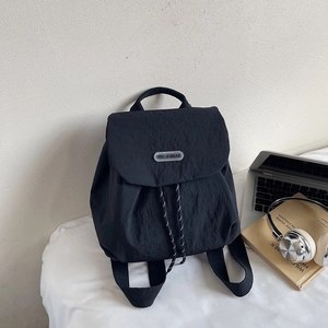 Lightweight black nylon backpack with flap closure and drawstring on a white desk
