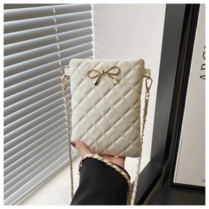 Detail of cream quilted crossbody bag featuring a golden metal bow and chain strap