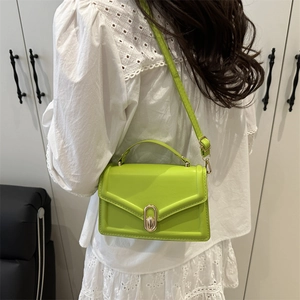 Fruitgroene crossbodytas van imitatieleer met ovale gouden gesp over een witte blouse