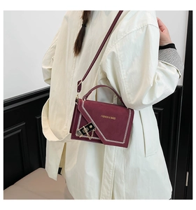 Macro shot of burgundy crossbody bag with white V-stitching and golden lock detail
