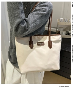 Close-up of off-white canvas tote bag with brown leather handles worn on shoulder