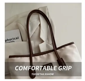 Detail of minimalist canvas tote with leather trim and brown rolled handles on white blazer