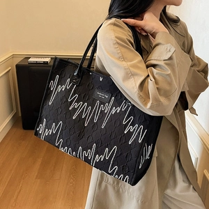Black quilted tote bag with white wave embroidery and shoulder straps shown on a model