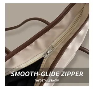 Detail of a smooth silver metal zipper on an off-white tote bag with brown leather piping