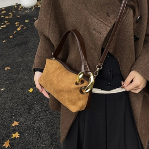 Sac baguette rétro en daim et cuir marron avec boucle dorée sur fond extérieur automnal