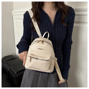Detail of cream mini backpack with woven texture and gold zippers worn by a model