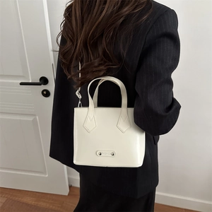 Bolso cubo chic de cuero blanco roto con asa y correa de hombro sobre un traje negro