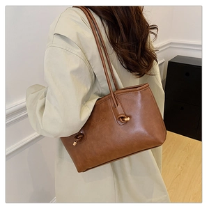 Detail of brown faux leather tote bag showing fashion text print and metal strap hardware