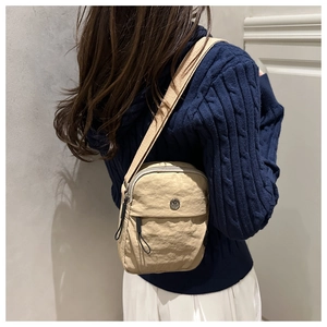Detail of a beige textured nylon crossbody bag with adjustable strap and metal logo