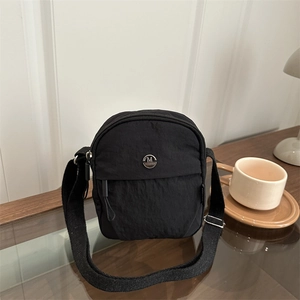 Gros plan d'un sac bandoulière en nylon noir avec logo M FASHION dans un décor de café