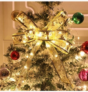 Close-up of a lighted golden mesh Christmas ribbon bow with warm LED stars on a snowy tree