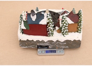 Close-up of a Christmas village resin ornament showing snow-covered details and LED power port