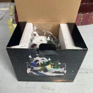 Detailed view of musical Christmas resin house with LED lights and safe foam packaging