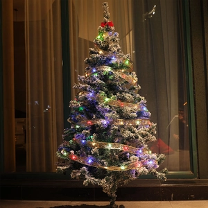 Snow-flocked Christmas tree with glowing LED gold ribbons and a large red bow top decoration
