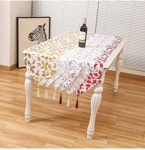 Close-up of white Christmas table runner with gold holly patterns and handmade tassels