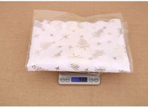 Detailed view of white Christmas table runner with gold tree print in package on scale