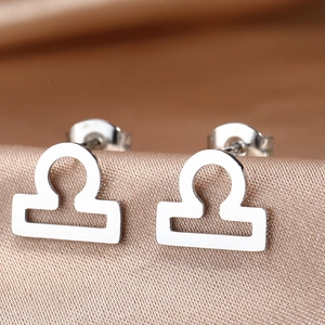 Macro shot of silver Libra zodiac stud earrings on champagne satin background