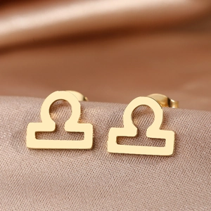 Close-up of golden Libra zodiac symbol stud earrings on an elegant champagne satin fabric