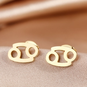 Detailed close-up of golden Cancer zodiac stud earrings on premium champagne silk fabric