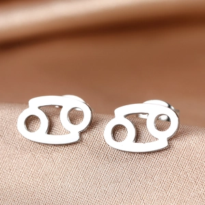 Macro shot of silver stainless steel Cancer zodiac stud earrings on champagne silk fabric