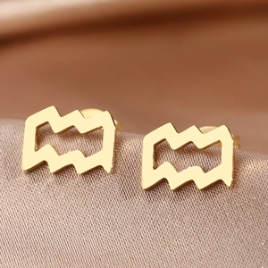 Macro shot of gold Aquarius zodiac stud earrings on champagne silk background