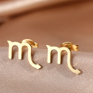 Close-up of golden Scorpio zodiac stud earrings on premium champagne silk fabric