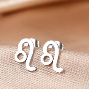 Macro shot of silver Leo zodiac sign stud earrings on smooth satin background
