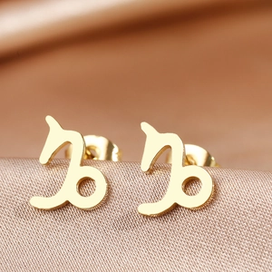 Detailed macro view of golden Capricorn zodiac stud earrings on silk fabric