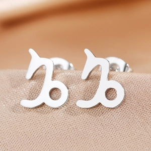 Macro shot of silver Capricorn zodiac stud earring on luxury silk fabric background