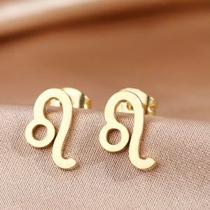 Macro shot of gold-plated Leo zodiac sign stud earrings on elegant champagne silk fabric