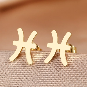 Detailed macro view of golden Pisces zodiac earrings on champagne silk background